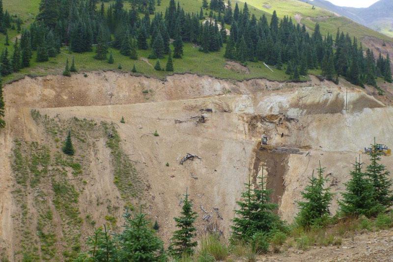 Looking across a valley, the opposite slope is a mostly dirt face with roads cut diagonally.
